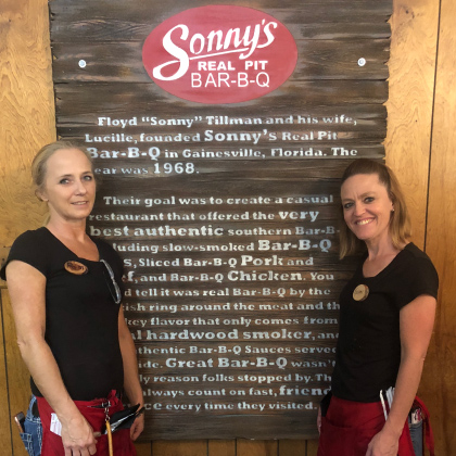 Servers stand next to the Sonny's BBQ mission sign